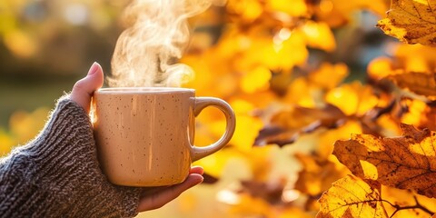 Wall Mural - A person holding a mug with steam coming from it, in front of fall foliage.