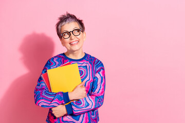 Wall Mural - Photo portrait of attractive senior woman hold copybooks look empty space dressed blue colorful clothes isolated on pink color background