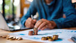 © khonkangrua - A person organizes coins and reviews financial charts on a desk, symbolizing budgeting, savings, and personal financial planning.