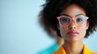 © Dulemegapixel - A confident woman wearing pink glasses and yellow attire poses against a minimalistic background, highlighting her sense of style and self-assured demeanor in a modern setting.