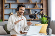 © Tetiana - Confident young man recording podcast at home while using laptop and microphone, engaging with audience through live streaming and headphones