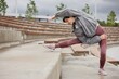 © Seventyfour - Side view of elderly woman in pink leggings stretching back muscles side bending over leg on huge concrete steps of amphitheater working out regularly in city park, copy space
