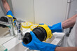 © AnastasiiaAkh - Hands in blue gloves washing vacuum cleaner filter with water in bathroom sink