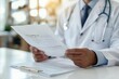 © Vera - close-up shot of a doctor's hand holding a medical report while sitting at a white desk in a clinic.