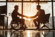 © Vera - powerful and inspiring image of two happy businessmen, one sitting on a wheelchair and one on a chair, shaking hands in front of a computer. The image symbolizes diversity and inclusion