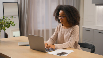 African american woman young millennial girl freelancer distant work from home quarantine female businesswoman in glasses working with laptop computer pc networking browsing online website in kitchen