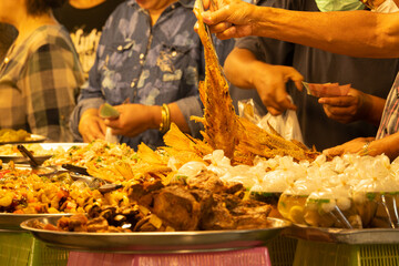 A group of people are gathered around a table with a variety of food, including a large piece of meat