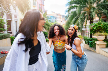 Three young women of diverse backgrounds joyfully holding hands and running down a sunny, palm-lined street in a vibrant, urban neighborhood. Their laughter and energy capture the spirit of friendship