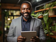 © Ekaterina - Portrait of a smiling man wearing a suit, holding a tablet in a modern office space with greenery in the background