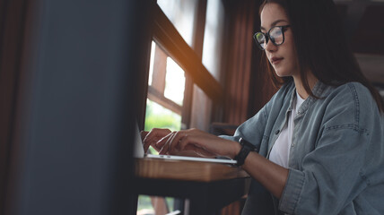 Wall Mural - Asian woman working on laptop computer at coffee shop. Young female freelancer online working at cafe. Student online studying, surfing the internet on laptop, e-learning, remote work, close up