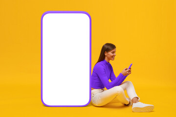 Wall Mural - Young woman sitting on floor near huge phone mock up for app