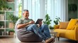 © Lahiru - A relaxed image of a middle-aged Indian man comfortably using a tablet while seated at home, surrounded by a cozy living space, ideal for lifestyle,