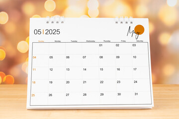 May 2025 desk calendar on wooden table with gold light bokeh background.