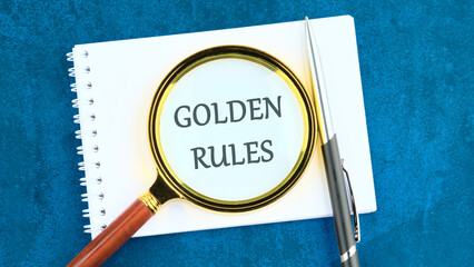 Conceptual golden rule symbol. Copy space. GOLDEN RULES words through the lens of a magnifying glass in a notebook and an abstract background