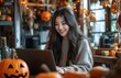 © yevgeniya131988 - Young Asian woman laughs while shopping online for a Halloween party in her decorated kitchen