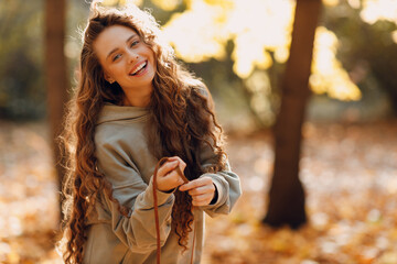 Wall Mural - Smiling young woman walking in autumn forest with the yellow leaves at sunset