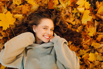 Smiling young woman lying on the autumn foliage in the forest with the yellow leaves