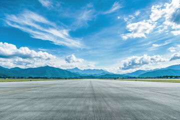 empty runway is leading to a mountain range under a blue sky with some clouds