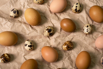 Quail eggs and brown chicken eggs on the background of crumpled brown paper in soft light