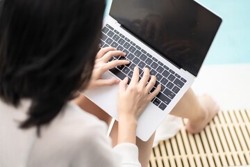 young asian female working beside swimingpool and typing computer labtop for social working every where relax vacation