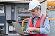 © amorn - Male electrician checking, repair, maintenance operation electric system in crane construction. Male electrician using laptop computer working with operation electric system in construction site
