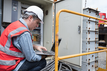 Male electrician checking, repair, maintenance operation electric system in crane construction. Male electrician using laptop computer working with operation electric system in construction site