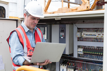 Male electrician checking, repair, maintenance operation electric system in crane construction. Male electrician using laptop computer working with operation electric system in construction site