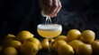 © Kartik - Cropped hand squeezing lemon juice to a glass of see-through foamy yellow cocktail. Lots of lemons. Moody still life. Refreshing drink.
