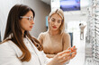© Dusko - Beautiful and fashionable woman choosing eyeglasses frame in modern optical store. Female seller specialist helps her to make right decision.