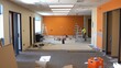 © AKE - An indoor construction site showcasing renovation work with ladders, paint buckets, and an orange accent wall.