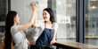© NAMPIX - Two young female successful entrepreneur in aprons smiling while making high five gesture and standing at their shop