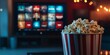 © Valerii Dekhtiarenko - Red and white striped popcorn bucket in focus with a TV streaming menu blurred in the background, evoking movie night vibes