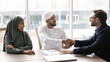 © fizkes - Positive European and Arabian entrepreneurs shaking hands at meeting table, smiling, getting agreement in collaboration, teamwork, discussing investment, partnership. Banner shot