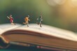 © Victor Bertrand - Miniature figures of children running on the pages of an open book, symbolizing the joy of imagination and adventure through reading.