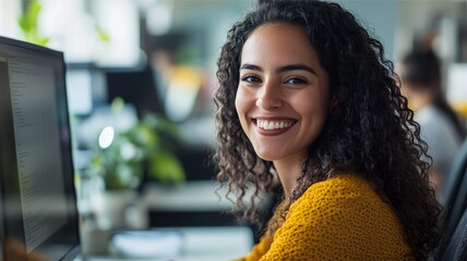 Portrait of an enthusiastic Hispanic young woman working on a computer in a bright, modern office. As a confident human resources agent, she smiles warmly, embodying professionalism and positivity.

