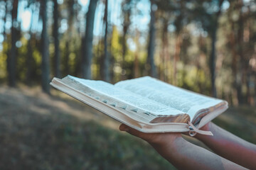 Christian illustration of a girl holding an open Bible against a forest backdrop