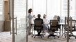 © fizkes - Arabian and European businesspeople discussing collaboration in modern office business meeting room, sitting at large table, talking to standing female group leader. Full length banner shot