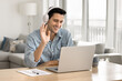 © fizkes - Cheerful attractive young Hispanic freelance professional man in headphones talking on video conference chat at laptop, waving hello, working at home, using Internet communication for online learning