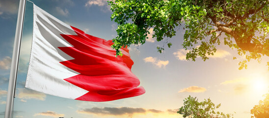 Bahrain national flag waving in the sky behind the tree. The flag blow in beautiful sunlight. Bahrain national flag for independence day.