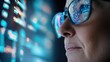 © Jasmina - Woman in glasses looks intently at a digital screen with data and code reflecting in the glasses