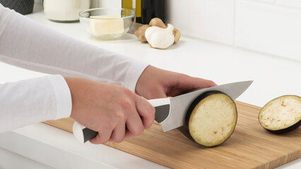 Wall Mural - Closeup of a person slicing an eggplant on a wooden cutting board.