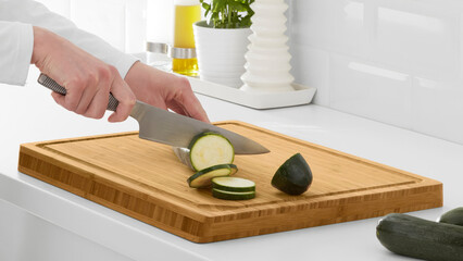 Wall Mural - Closeup of a person slicing cucumbers on a wooden cutting board.