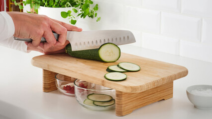 Wall Mural - Closeup of a person slicing cucumbers on a wooden cutting board.