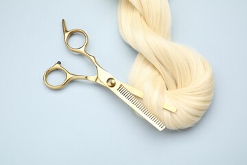 Wall Mural - Blonde hair strand and professional scissors on light grey background, top view