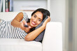© peopleimages.com - Happy woman, portrait and watching tv with remote on sofa for entertainment, relax or movie at home. Young female person or smile in comfort for online subscription, shows or series on couch at house
