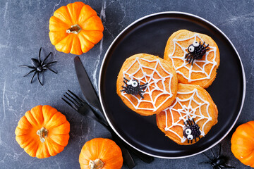 Poster - Spooky Halloween spider web pumpkin pancakes with blackberry spiders. Overhead view on a black plate against a dark stone table background.