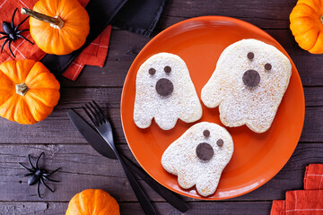 Poster - Cute Halloween ghost pancakes. Top view on an orange plate against a dark wood table background.