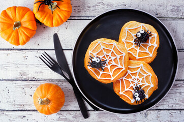 Aufkleber - Spooky Halloween spider web pumpkin pancakes with blackberry spiders. Above view on a black plate against a rustic white wood table background.