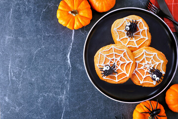 Wall Mural - Fun Halloween spider web pumpkin pancakes with blackberry spiders. Top down view on a black plate against a dark stone table background with copy space.