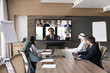 © fizkes - Multiethnic business team of Arab and European colleagues meeting on online video conference call. Diverse directors sitting at table, looking at display with speaking affiliate company employees